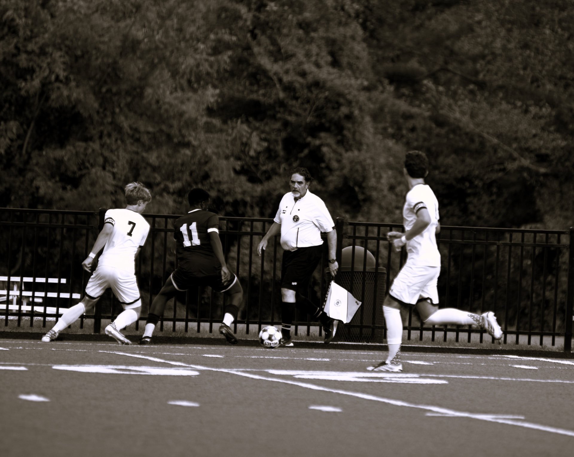 Players chase the ball along the sideline past the linesman