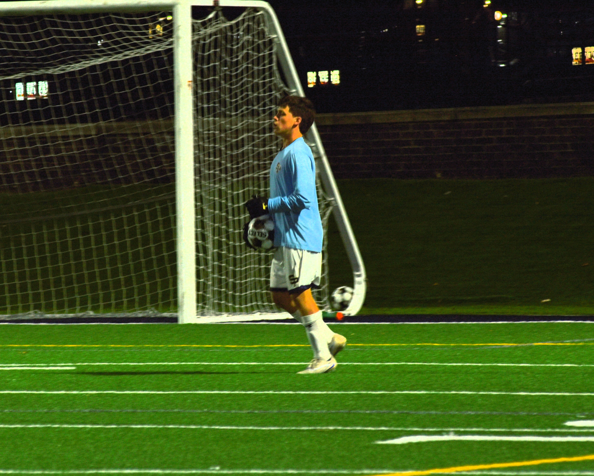 Goalkeeper watches play beside the goal at night