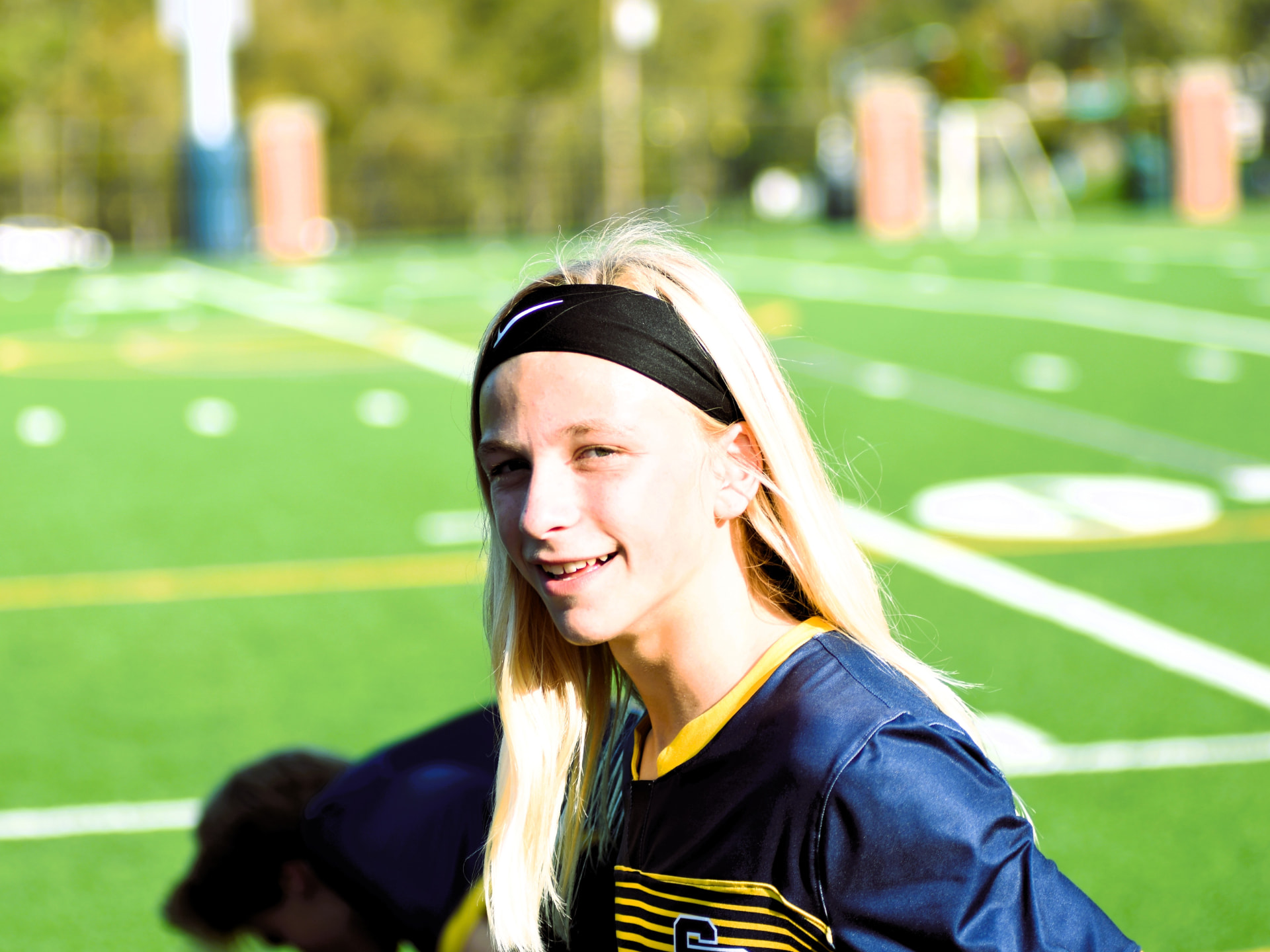 A JV Crusader in a black headband smiles on the field