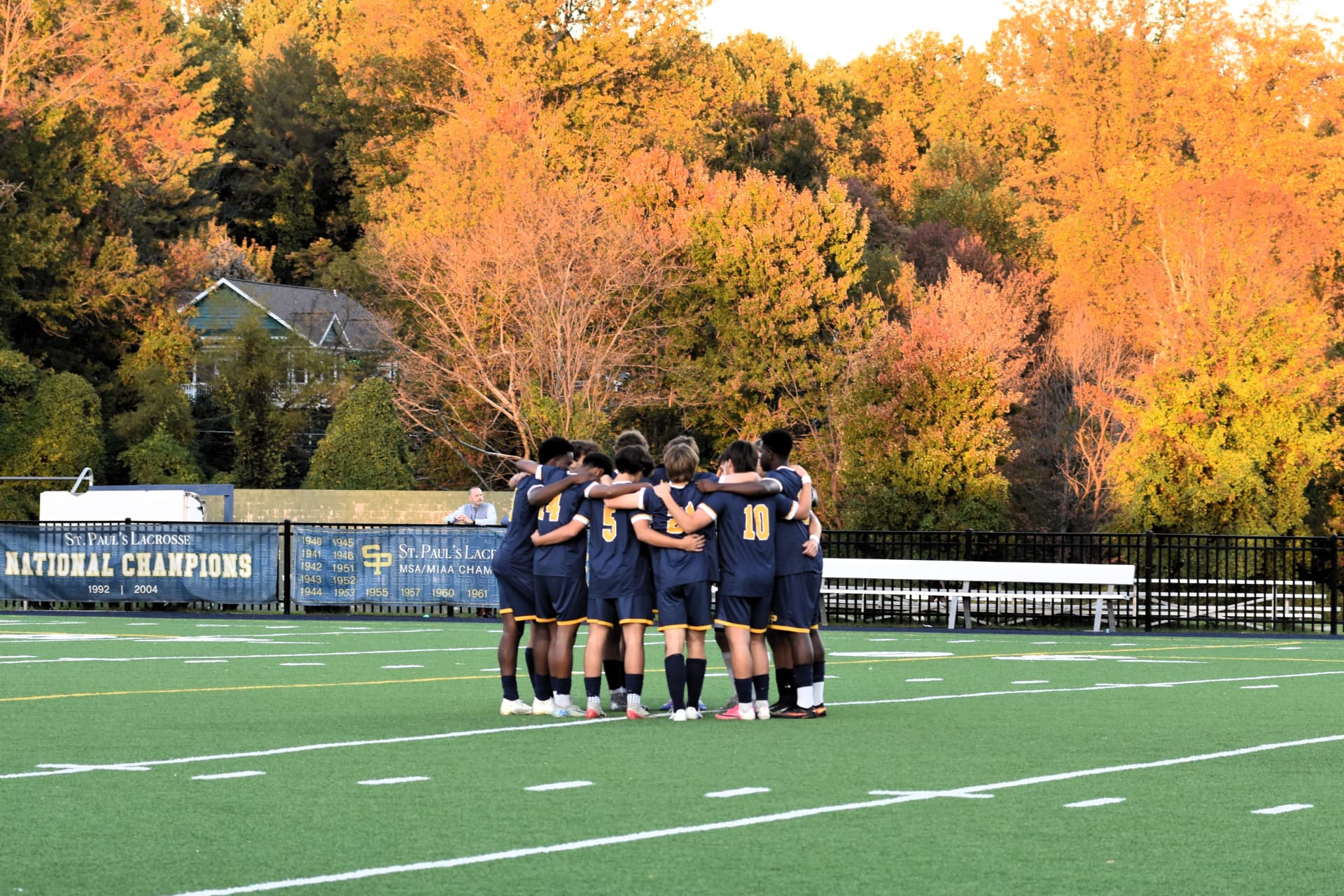 St. Paul's team huddles on the field beneath autumn trees