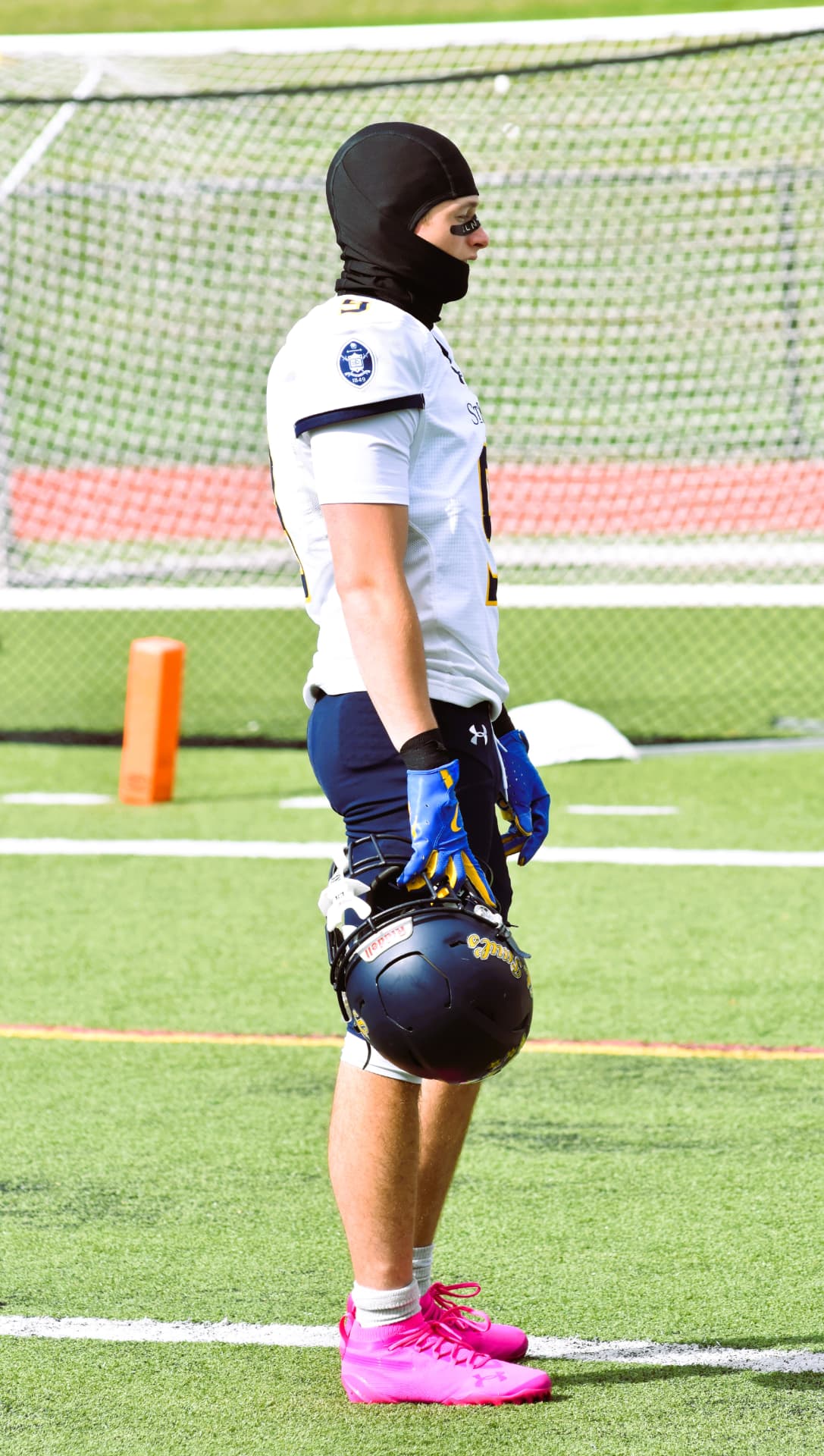 A Crusader stands in pink cleats holding his helmet